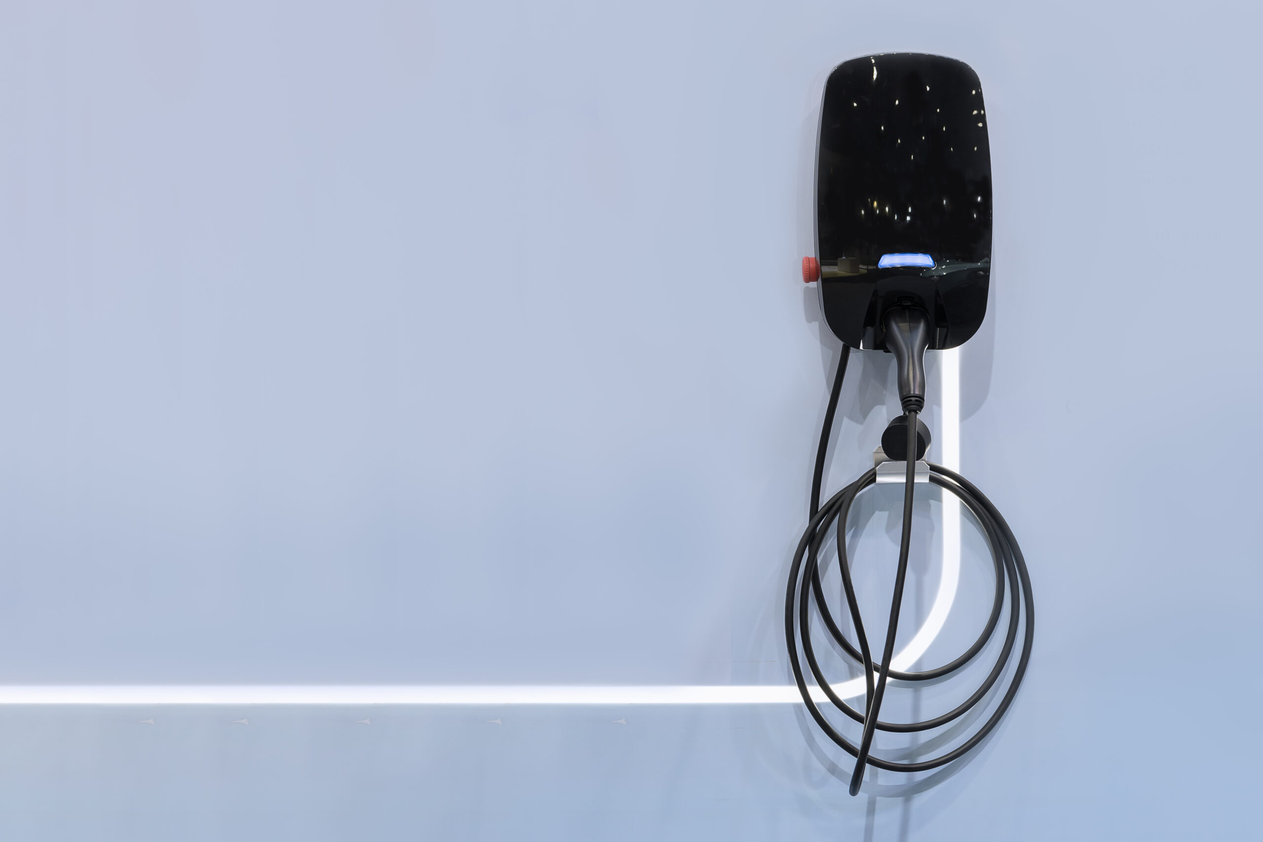 Electric vehicle charging station mounted on a light gray wall. A coiled cable hangs below the black charging unit.